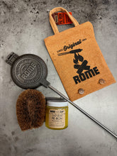 Load image into Gallery viewer, Round Pie Iron & Seasoning Bundle from Rome, including round pie iron, storage cover, seasoning oil, and cleaning brush, displayed on a gray surface - closeup view