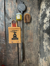 Load image into Gallery viewer, Round Pie Iron & Seasoning Bundle from Rome, including round pie iron, storage cover, seasoning oil, and cleaning brush, displayed on a gray surface - view 3