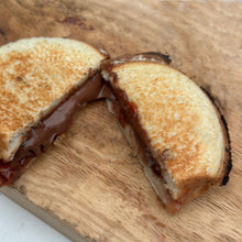 Load image into Gallery viewer, Round cooked mountain pie sandwich cut in half with jelly and nutella